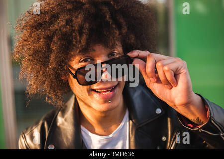 Handsome young black man with afro hairstyle and sunglasses looking to the camera and smiling, closeup with urban background Stock Photo