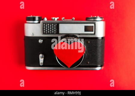 old vintage photo camera with red heart on it. red background.for decor and design. valentines greeting card. concept love and romance at photographs. Stock Photo