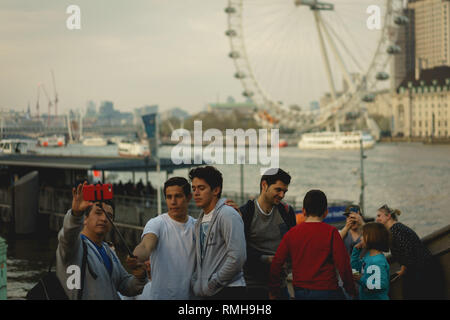 London, UK - April, 2018. Young tourists taking selfies in Westminster with the river Thames and the London Eye on the background. Stock Photo
