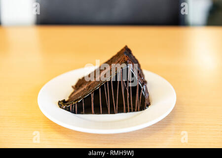 A slice of chocolate cake with icing served on a white plate on an office desk, UK. Stock Photo