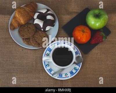 A coffee cup and a plate of black slate with a green apple, a tangerine and a strawberry and one plate with one croissant, one chocolate donut and coo Stock Photo