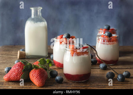 Still life of homemade yogurt with strawberry jam and pieces of fruit on a wooden board Stock Photo