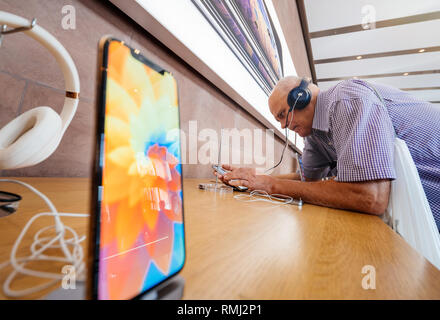 STRASBOURG, FRANCE - SEP 21, 2018: Side view of funny curious senior man testing Apple Beats by Dr Dre headphones with Apple Music on the new iPhone Xs Max smartphones in modern Apple Store - modern computer store Stock Photo