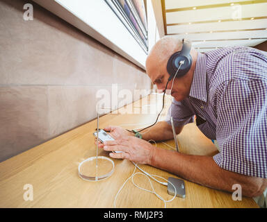 STRASBOURG, FRANCE - SEP 21, 2018: Side view of funny curious senior man testing Apple Beats by Dr Dre headphones with Apple Music on the new iPhone Xs Max smartphones in modern Apple Store  Stock Photo