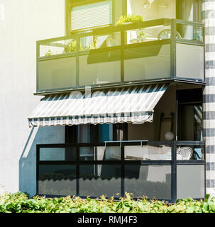 Beautiful stripped balcony patio awning on the facade of a French apartment building ready for the summer and hot sun - two floor building with big yellow sunlight flare Stock Photo