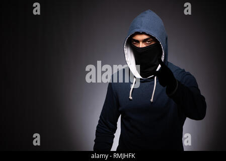 Young gangster in hood on grey background Stock Photo