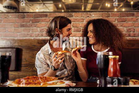 Portrait of young man and woman sitting at fast food restaurant eating with pizza. Cheerful couple enjoying eating pizza at cafe. Stock Photo