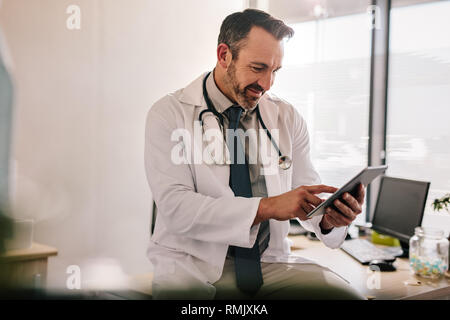 Mature male doctor using tablet computer at his office. General practitioner using digital tablet at his clinic. Stock Photo