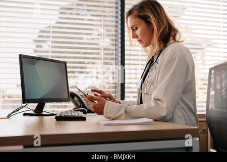 Female physician using a digital tablet in the clinic. Female doctor sitting at her desk and working on her tablet pc in her office. Stock Photo