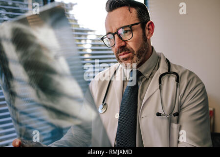 Concerned male doctor looking at chest x ray in his office. Doctor looking at scan, examining X-ray of patient lungs. Stock Photo