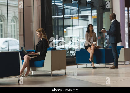 Businesswoman using laptop while coworkers interacting with each other in the lobby Stock Photo