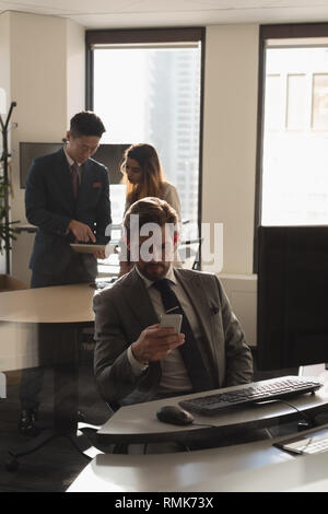 Man using mobile phone while coworkers discussing over digital tablet Stock Photo