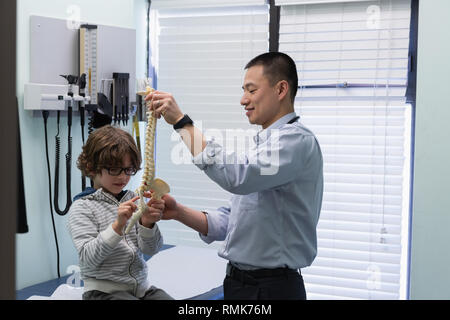 Young asian male doctor showing vertebral column model to caucasian boy patient Stock Photo