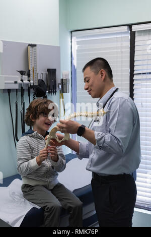 Young asian male doctor showing vertebral column model to caucasian boy patient Stock Photo