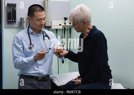 Young Asian male doctor measuring blood sugar level with glucometer of senior woman Stock Photo