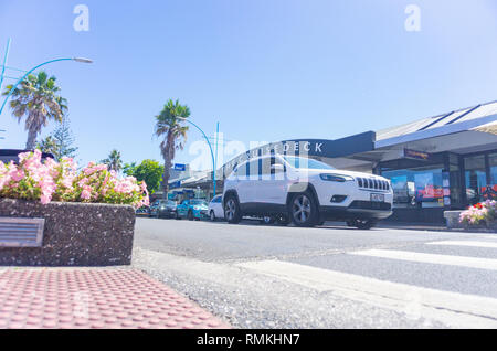 MOUNT MAUNGANUI NEW ZEALAND - FEBRUARY 8 2019: Maunganui Road in main shopping area with passing vehicles and people and black and white CruiseDeck sh Stock Photo