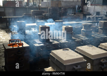 Smoke arises from hot moulds of cast iron at the end of a pour in a foundry Stock Photo