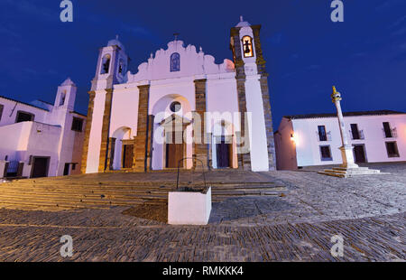 Central square with medival church, pillory and historic white washed buildings by night Stock Photo