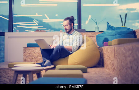 software developer writing programming code using laptop computer while sitting on lazy bag in modern startup office Stock Photo