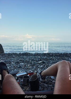 View from a tent at beach, human legs lying in tourist tent with view of the sea, pebble beach Stock Photo