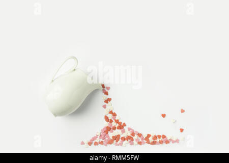 Multicolored sugar candy hearts imitating pouring liquid coffee tee from white milk jug. Creative flat lay. Valentine charity love donation generosity Stock Photo