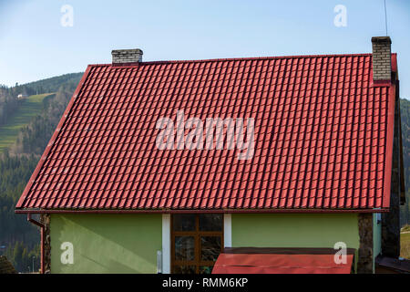 Detail of new modern house cottage corner with stucco walls decorated with natural stones, red shingled roof and rain gutter pipe system on blurred sp Stock Photo