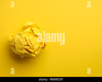 Crumpled yellow paper ball on a yellow background with space for text or image, view from above Stock Photo