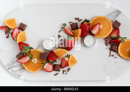 Flat lay composition of a mix of strawberries, orange, chocolate and candles on a bright marble background Stock Photo