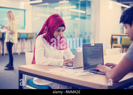 successful black muslim business woman having a meeting with her indian male colleague working on the laptop at modern startup office Stock Photo