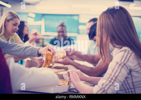 Friendly diverse multiethnic business team eating sharing pizza together in startup office, multiracial coworkers staff group enjoying break talking l Stock Photo