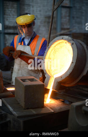Foundrymen pour molten iron into moulds for making fire grates. (Shot in available light with shallow depth of field.) Stock Photo