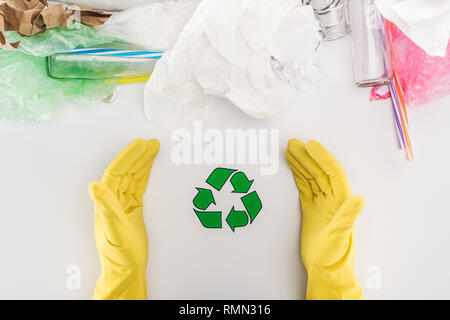 Partial view of man in yellow rubber gloves among glass bottles, plastic bags, paper and plastic tubes with recycling symbol Stock Photo