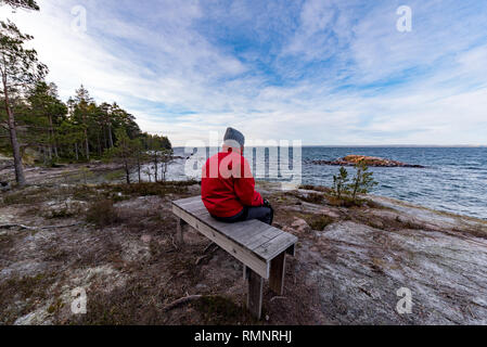 man in red jacket sitting on a bench overlooking lake vattern Stock Photo