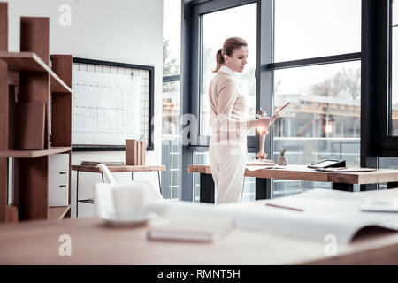 Interview time. Successful human resources manager feeling proud while standing near window looking through curriculum vitas Stock Photo