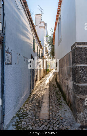Winding narrow cobblestone alley leading away between traditional whitewashed stone houses in Cascais Portugal Stock Photo