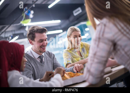 Friendly diverse multiethnic business team eating sharing pizza together in startup office, multiracial coworkers staff group enjoying break talking l Stock Photo