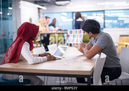 successful black muslim business woman having a meeting with her indian male colleague working on the laptop at modern startup office Stock Photo