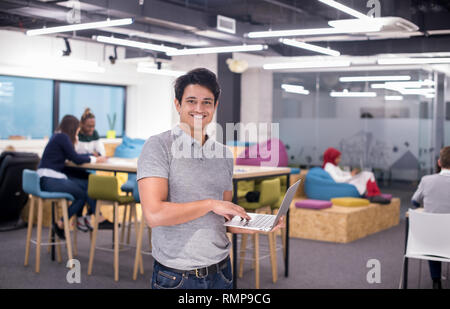 portrait of young indian businessman using laptop computer with his multiethnic business team in background at busy startup office Stock Photo