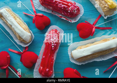 assorted eclairs with various flavor on blue wooden background with velvet hearts decor Stock Photo