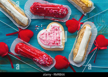 eclairs and heart shaped cookie with valentines day decor on blue wooden background Stock Photo