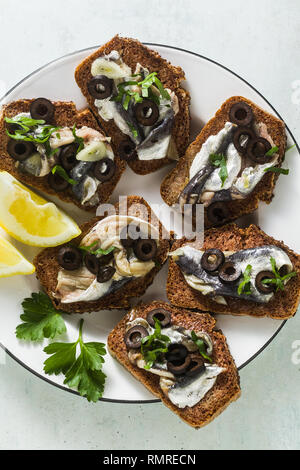 sandwiches with sardines marinated in olive oil with garlic and rye bread. summer light italian appetizer with lemon and parsley Stock Photo