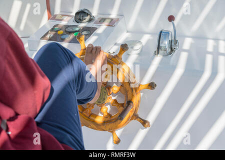 People at the helm of a white yacht. A man Arab controls the yacht. Foot on the yacht steering wheel. Stock Photo