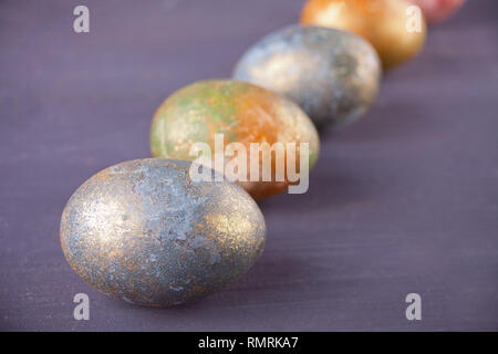 Row of colorfully nacreous Easter eggs on black wooden background Stock Photo