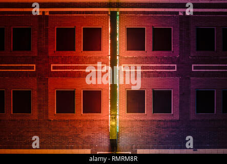 Building with black windows at night illuminated by a red and green neon sign Stock Photo