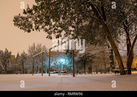 Empty park swings during a Winter night, after a few snow heavy hours. Quiet outdoor place in Bucharest, Romania, with snow covered trees and diffused Stock Photo