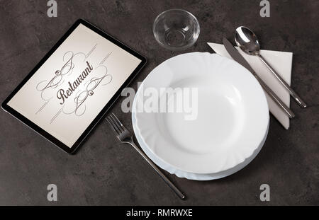Tablet with stylish restaurant logo and laid table  Stock Photo