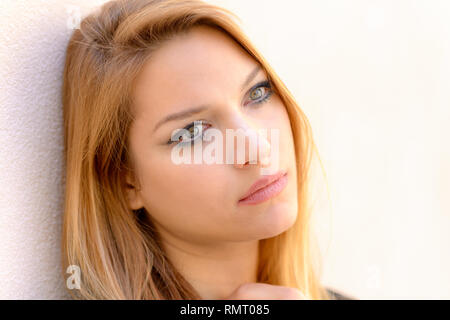 Attractive calm woman looking quietly as she leans against a wall with her hand to her throat Stock Photo