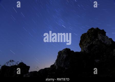 Star trails representing rotation of celestial sphere with rocks on a foreground. Stock Photo