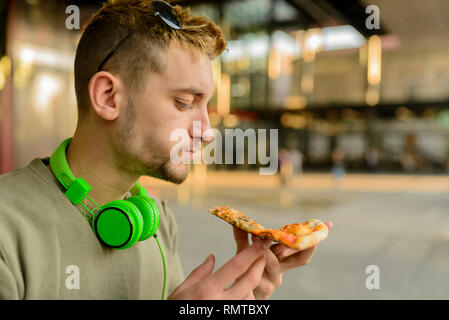 Handsome young man with headphones eating pizza in the city street Stock Photo