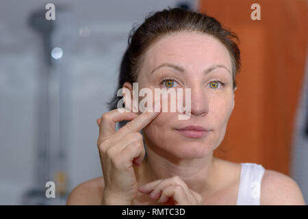 Woman checking her skin in the mirror for signs of ageing and wrinkles pulling on the skin of her cheek Stock Photo